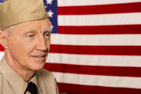 Senior man, army veteran with USA flag. He wears a WWII military uniform. Patriotism, honor, respect.