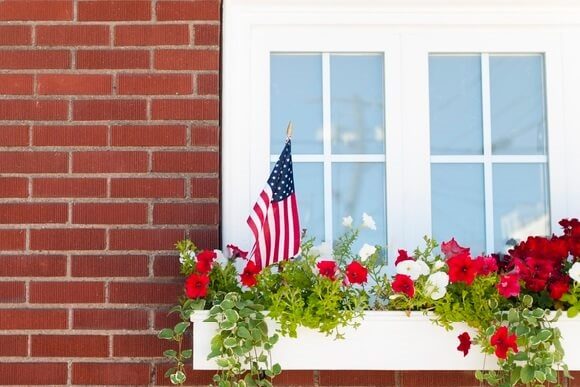 Exterior of a brick home showing a window sill planter with flowers and an American flag.